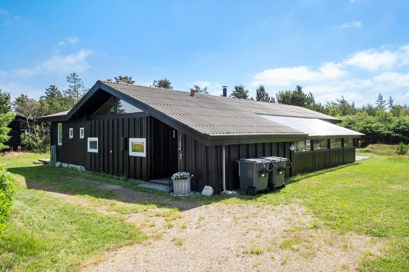 Ein dunkles Holzhaus mit Dach und Fenstern, umgeben von Gras und Bäumen.