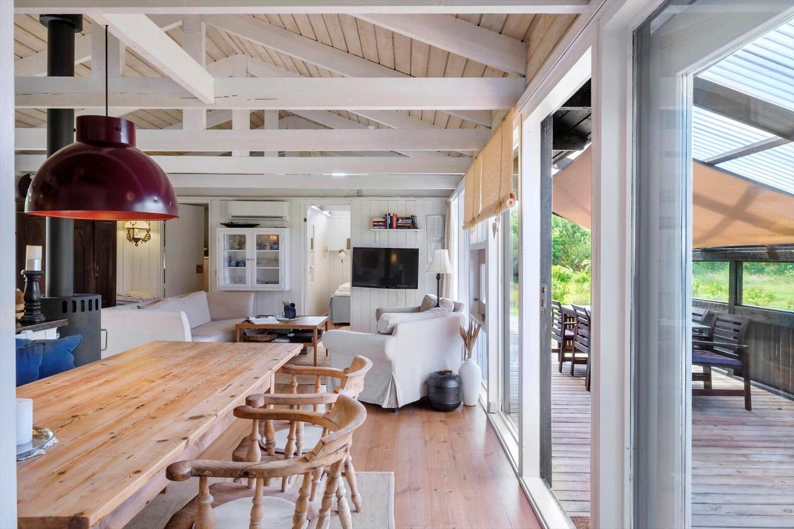 Wohn- und Essbereich mit Holzdecke, Tisch und Stühlen, Fernseher und Blick auf die Terrasse.