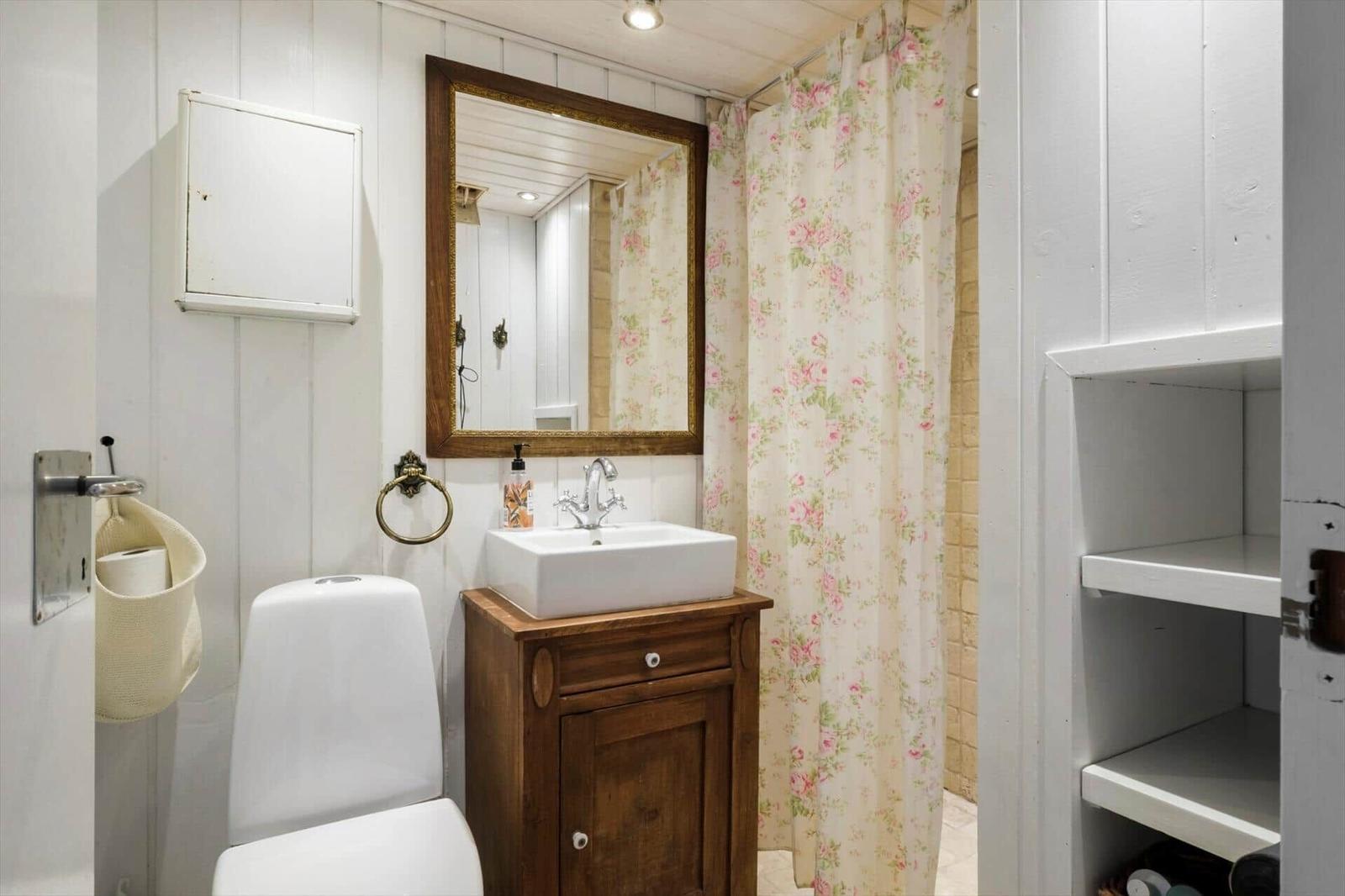 Badezimmer mit Toilette, Waschbecken und Dusche mit floraler Vorhang.