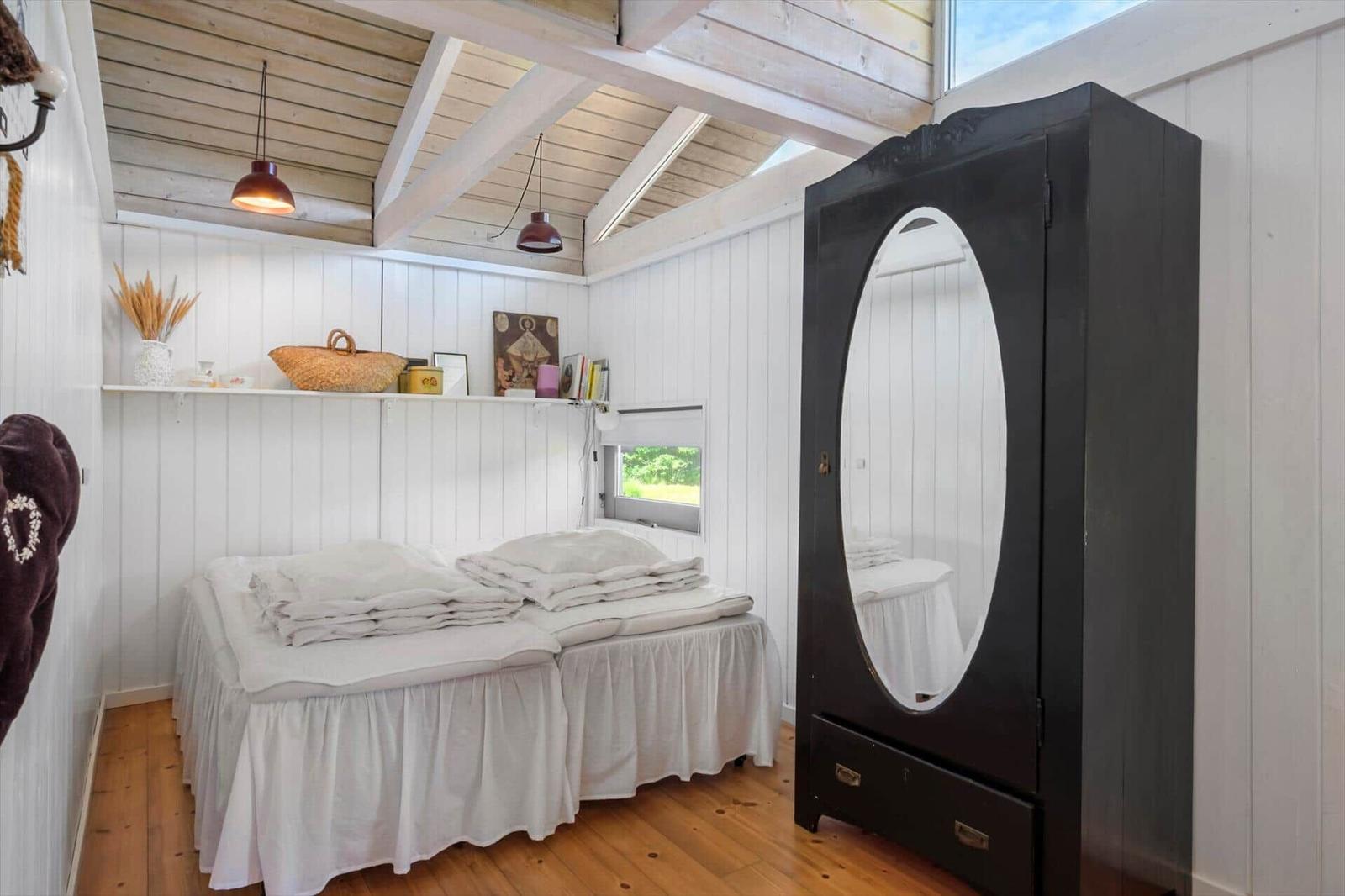 Schlafzimmer mit Doppelbett, schwarzer Kommode und Holzboden. Weiße Wände und hölzerne Decke.