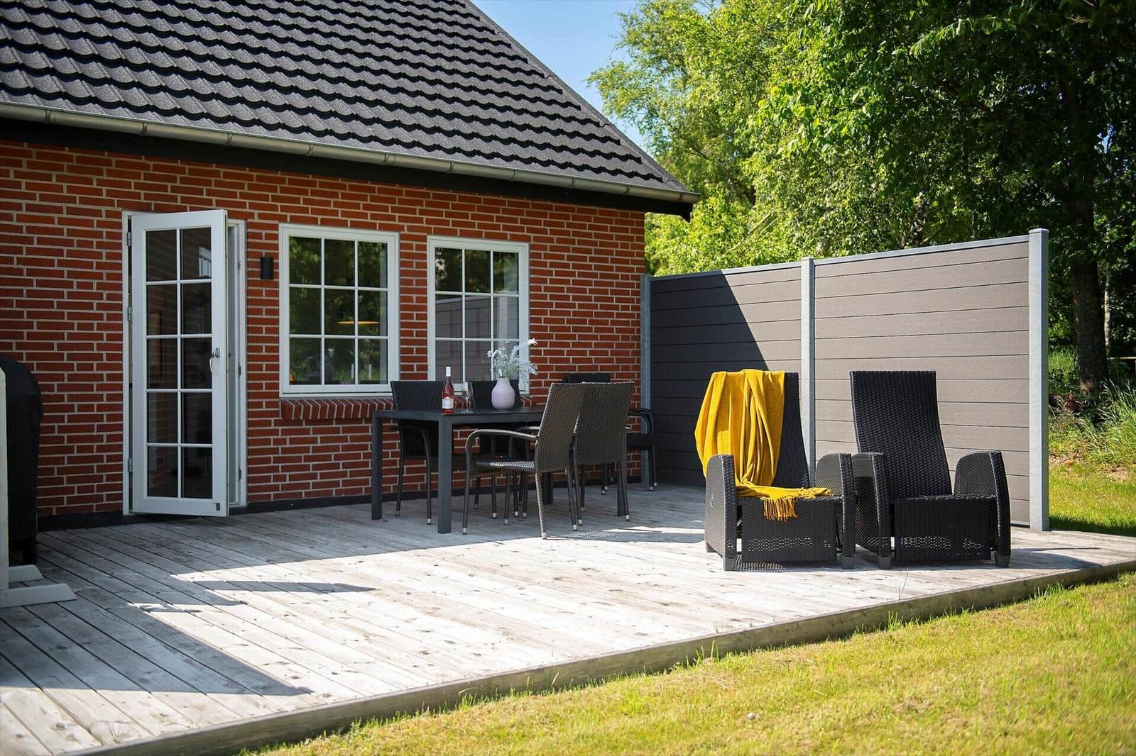 Terrasse mit Tisch, Stühlen und Liegestühlen vor einem roten Backsteinhaus.