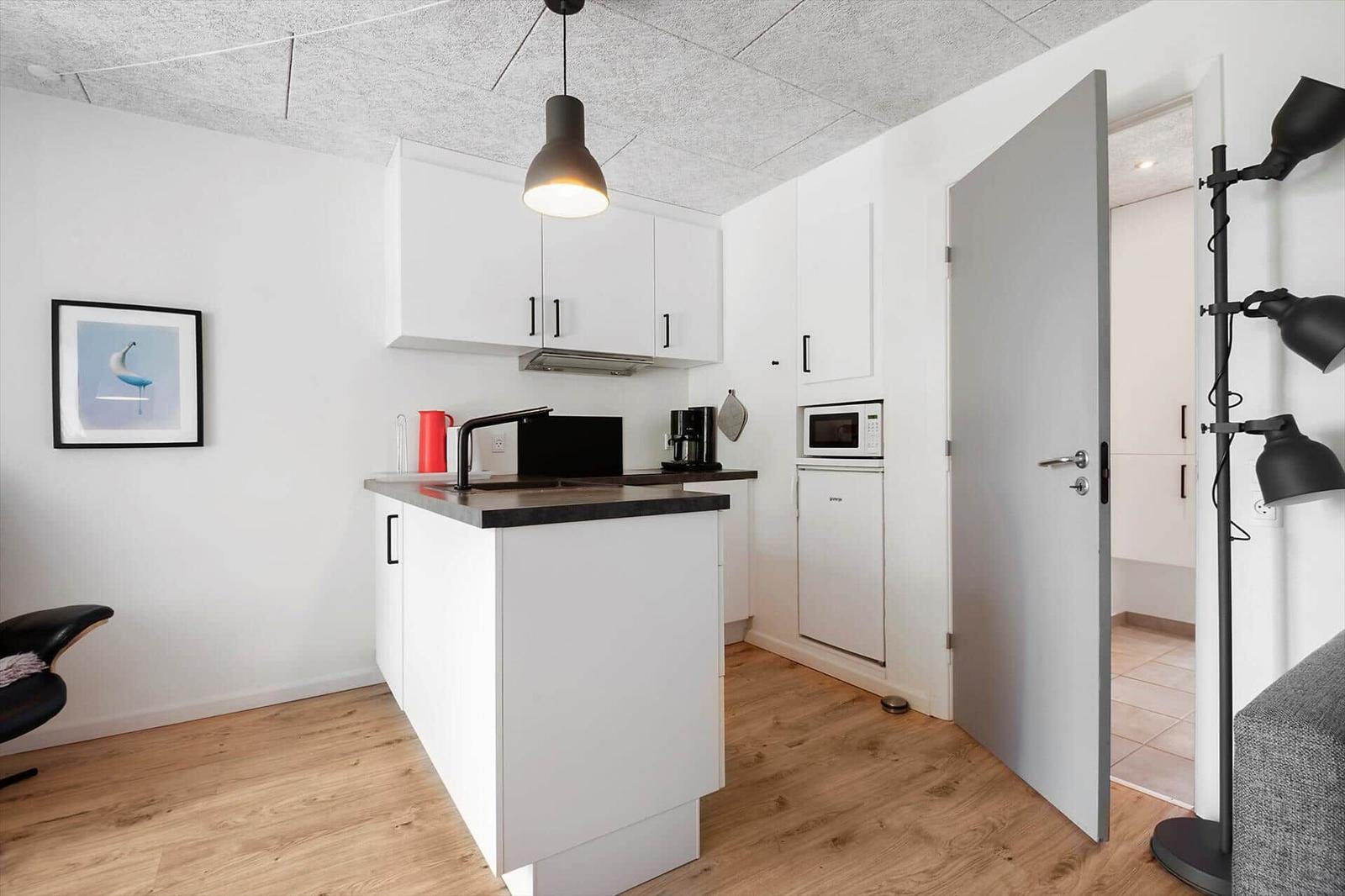Küche mit Arbeitsplatte, Kühlschrank und Mikrowelle. Tür führt in ein anderes Zimmer.
