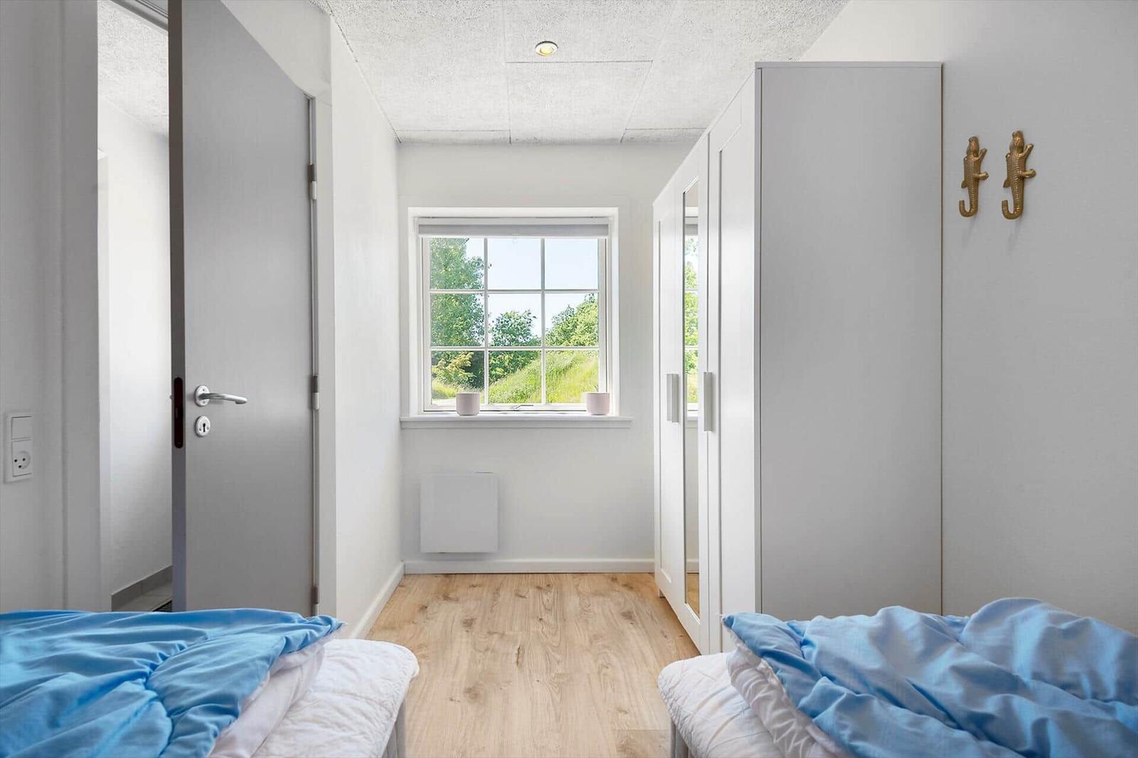 Zimmer mit zwei Betten, Fenster mit Blick auf Grün, weißer Schrank und Holzboden.