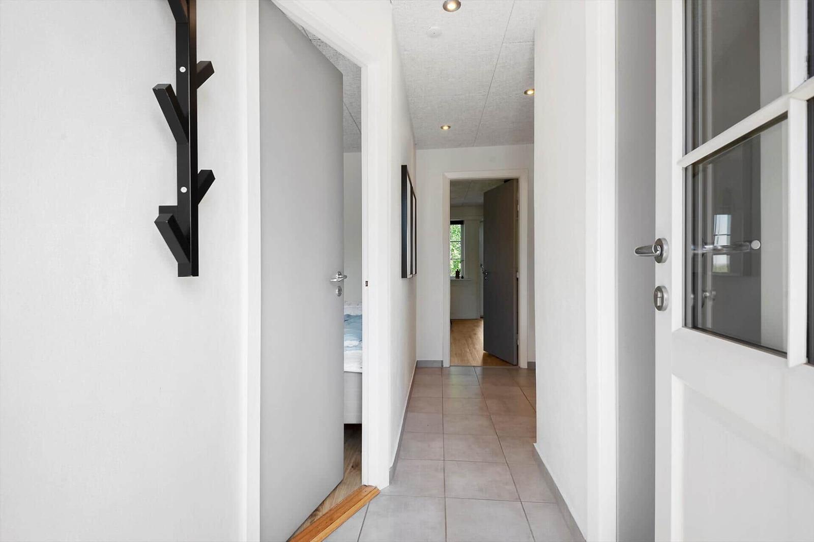 Flur mit Tür zu Schlafzimmer und Fenster. Wandhalter und Bodenfliesen sichtbar.