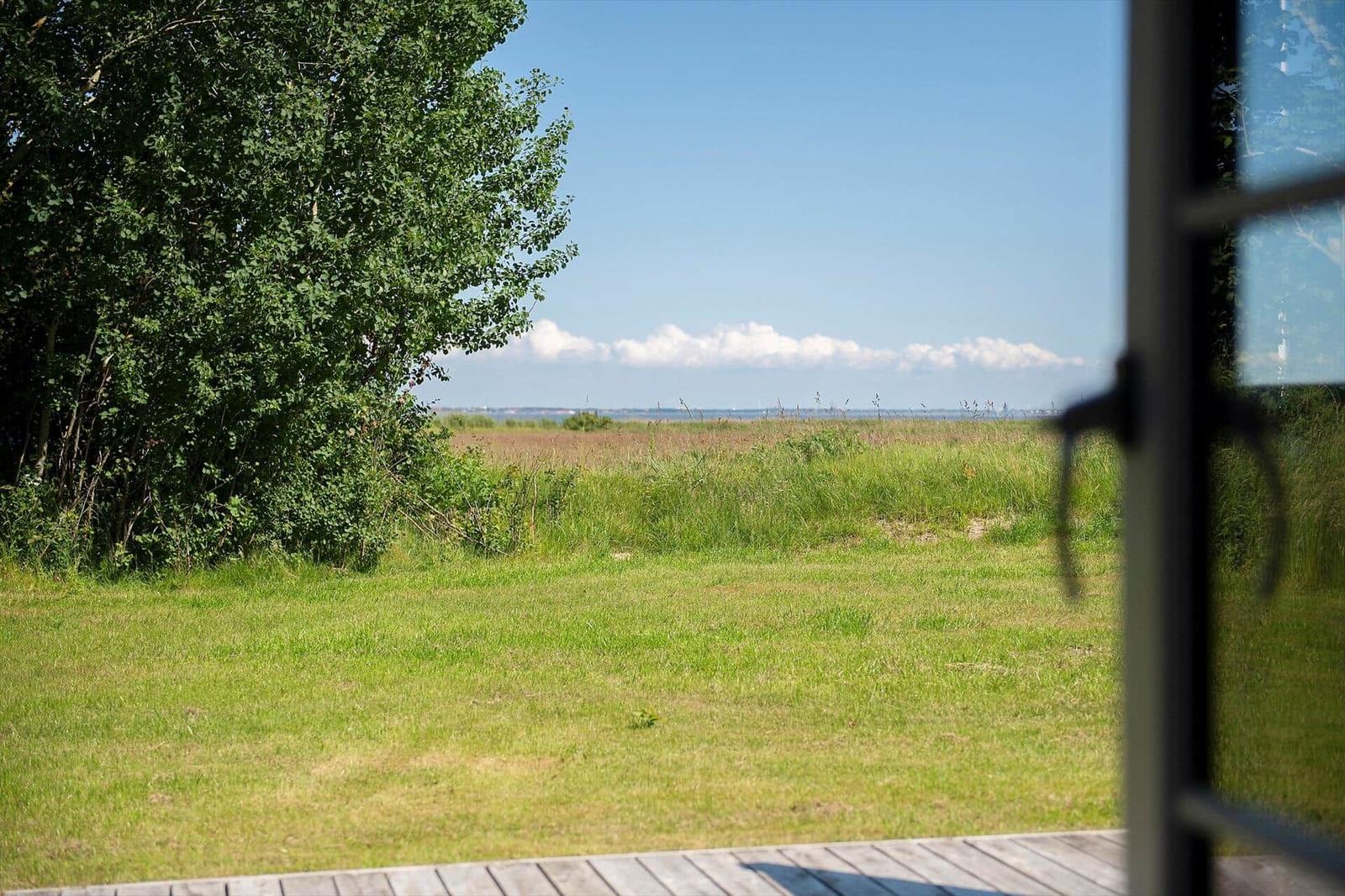 Von der Terrasse aus Blick auf grünes Gras und einen Wald. Im Hintergrund ist ein Fluss mit blauem Himmel zu sehen.
