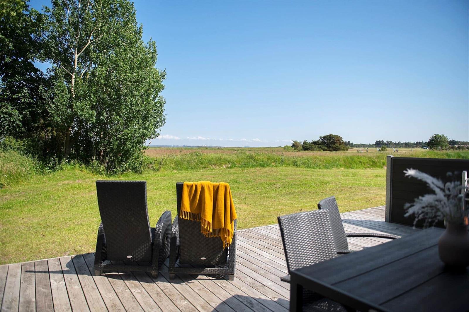 Terrasse mit Loungemöbeln und Blick auf grünes Feld unter blauem Himmel.