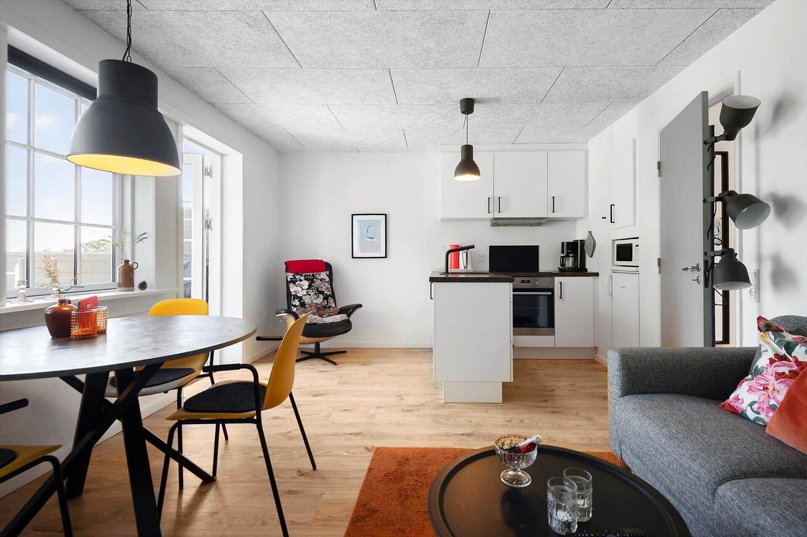 Wohnung mit Essbereich, Küche und Sofa. Holzboden, große Fenster und moderne Beleuchtung.