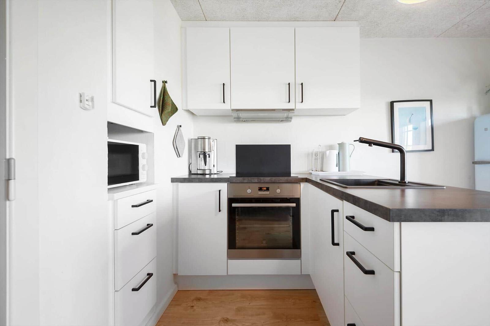 Küche mit weißen Schränken, dunklem Arbeitsplatz und integriertem Backofen.