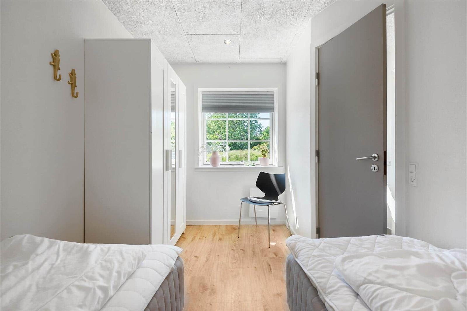 Zwei Betten, ein Schrank, ein Stuhl und ein Fenster mit Blick auf Grün.