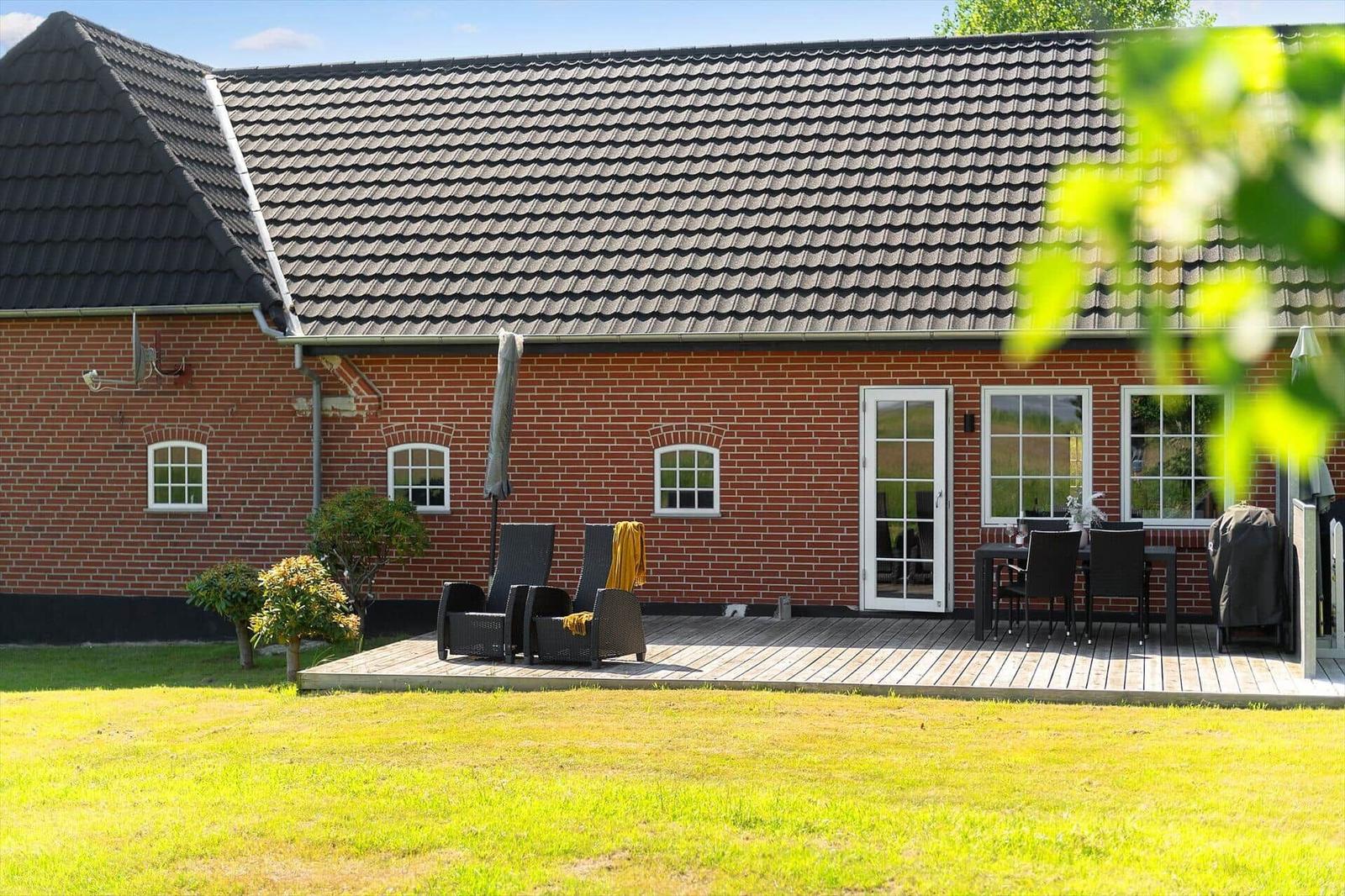 Roter Backsteinbau mit Terrasse, Garten und Sitzgelegenheiten.