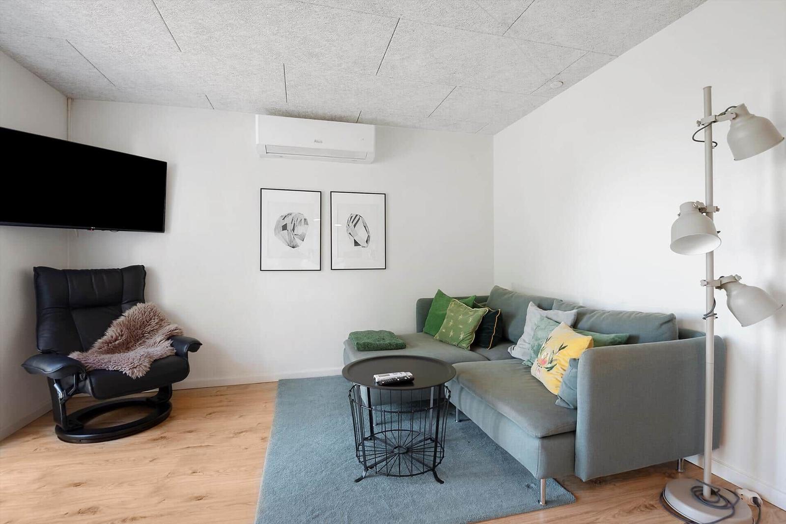Wohnzimmer mit Sofa, Sessel, Fernseher und Stehlampe.