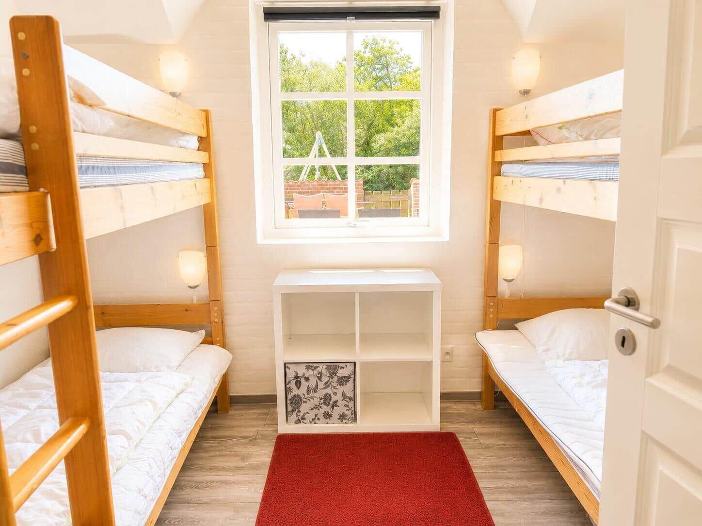 Zwei Etagenbetten, ein Fenster, ein weißer Schrank und ein roter Teppich.