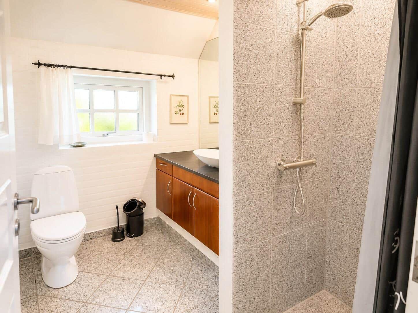 Badezimmer mit Dusche, Toilette und Waschbecken unter Fenster.