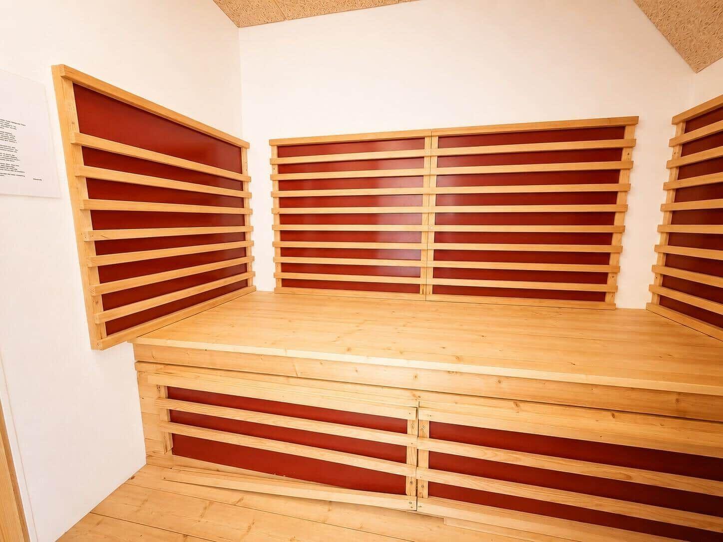 Sauna mit Holzbank und roten Paneelen an den Wänden.