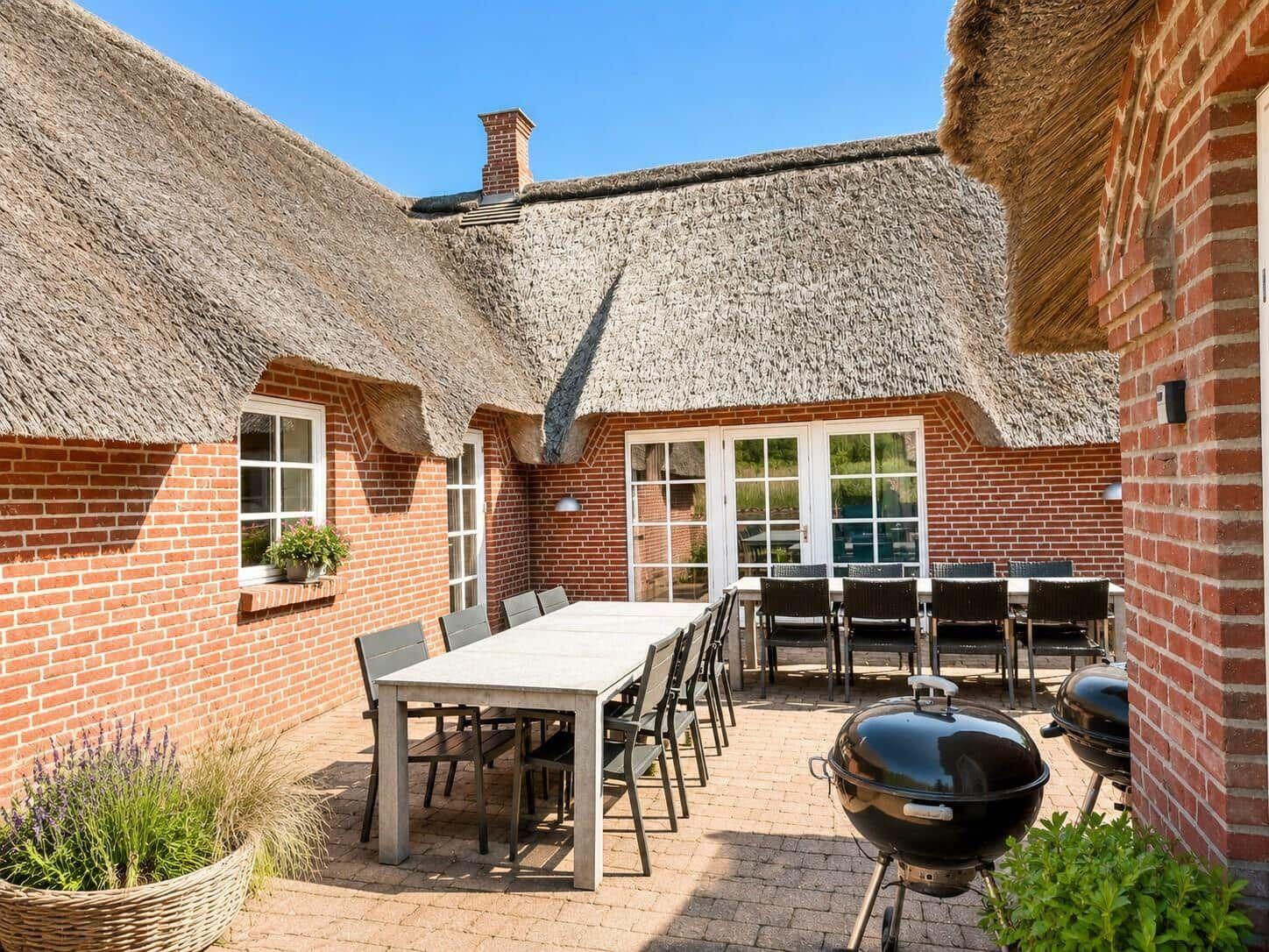 Terrasse mit Tisch, Stühlen und Grill unter strohgedecktem Dach.