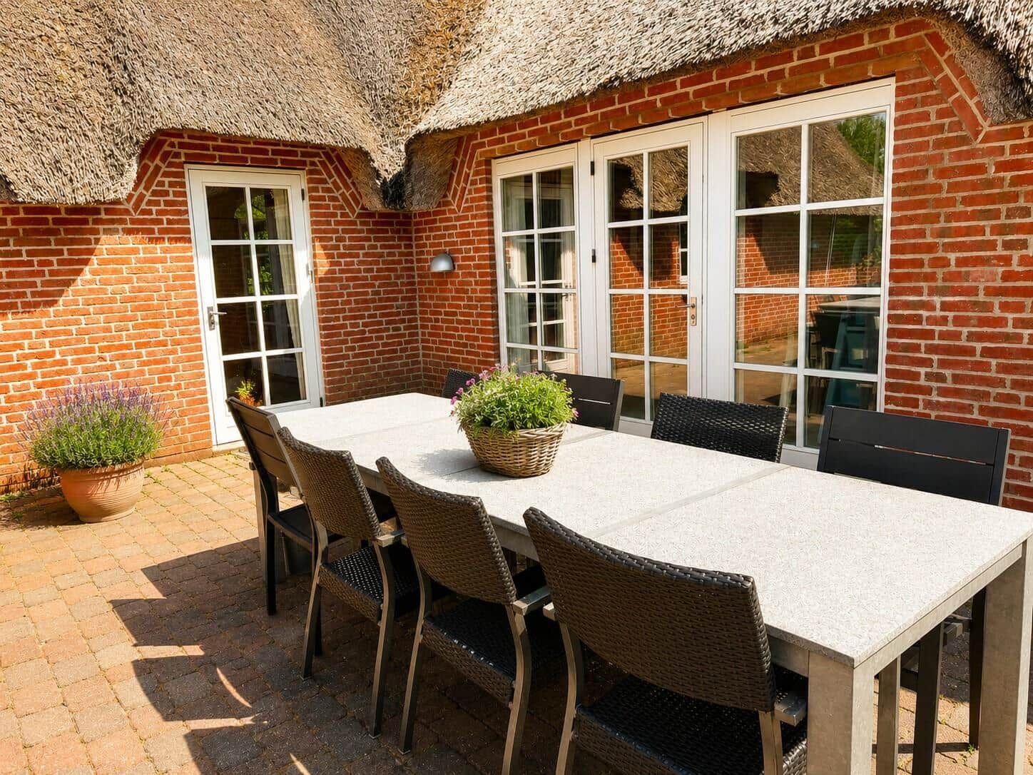 Terrasse mit Tisch und Stühlen vor rotem Backsteinhaus mit Strohdach.