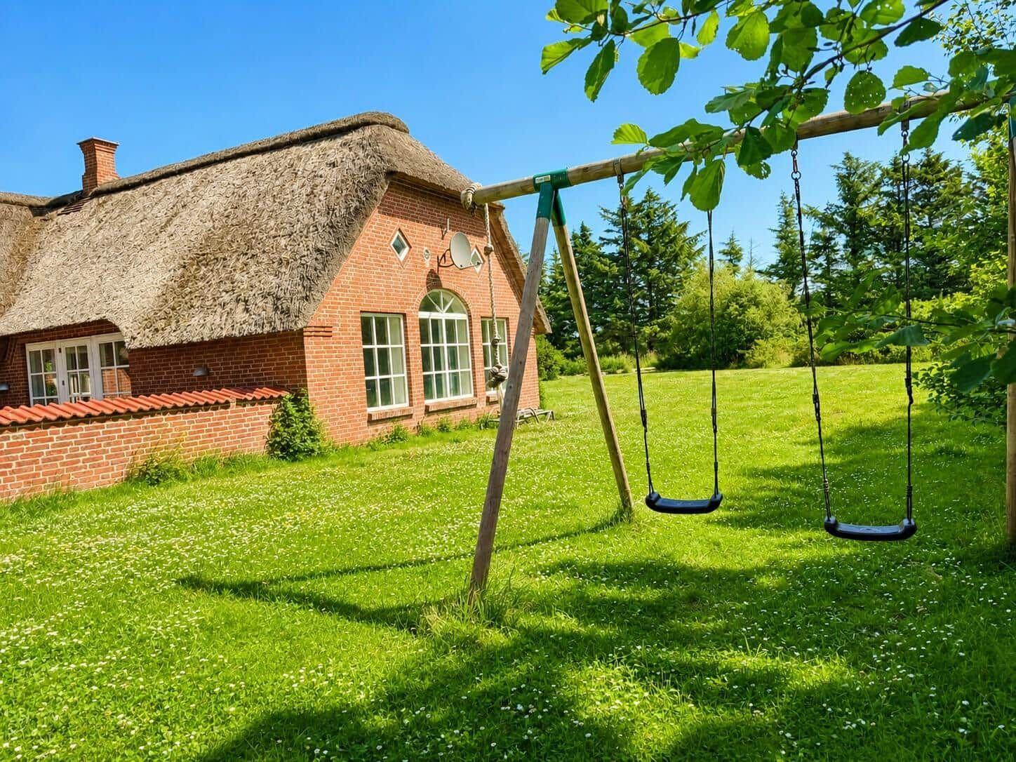 Haus mit Strohdach und Spielplatz mit Schaukel im Garten.