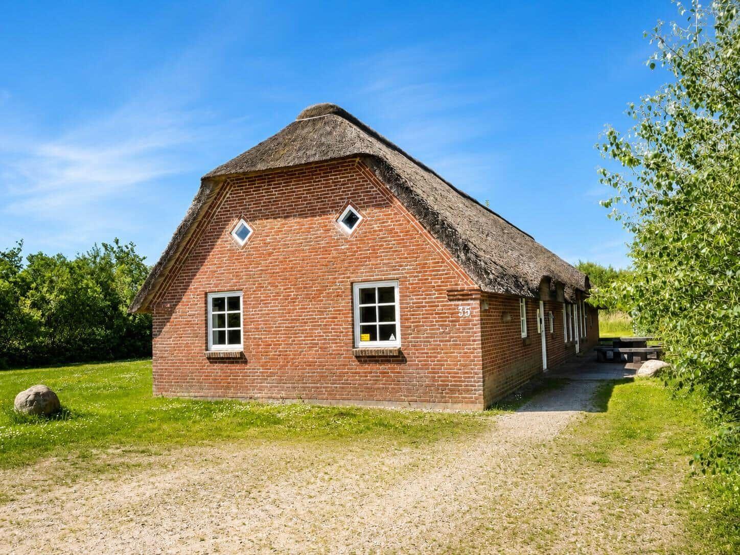 Rotes Backsteingebäude mit Strohdach und Fenstern. Grasfläche und Bäume umgeben das Haus.