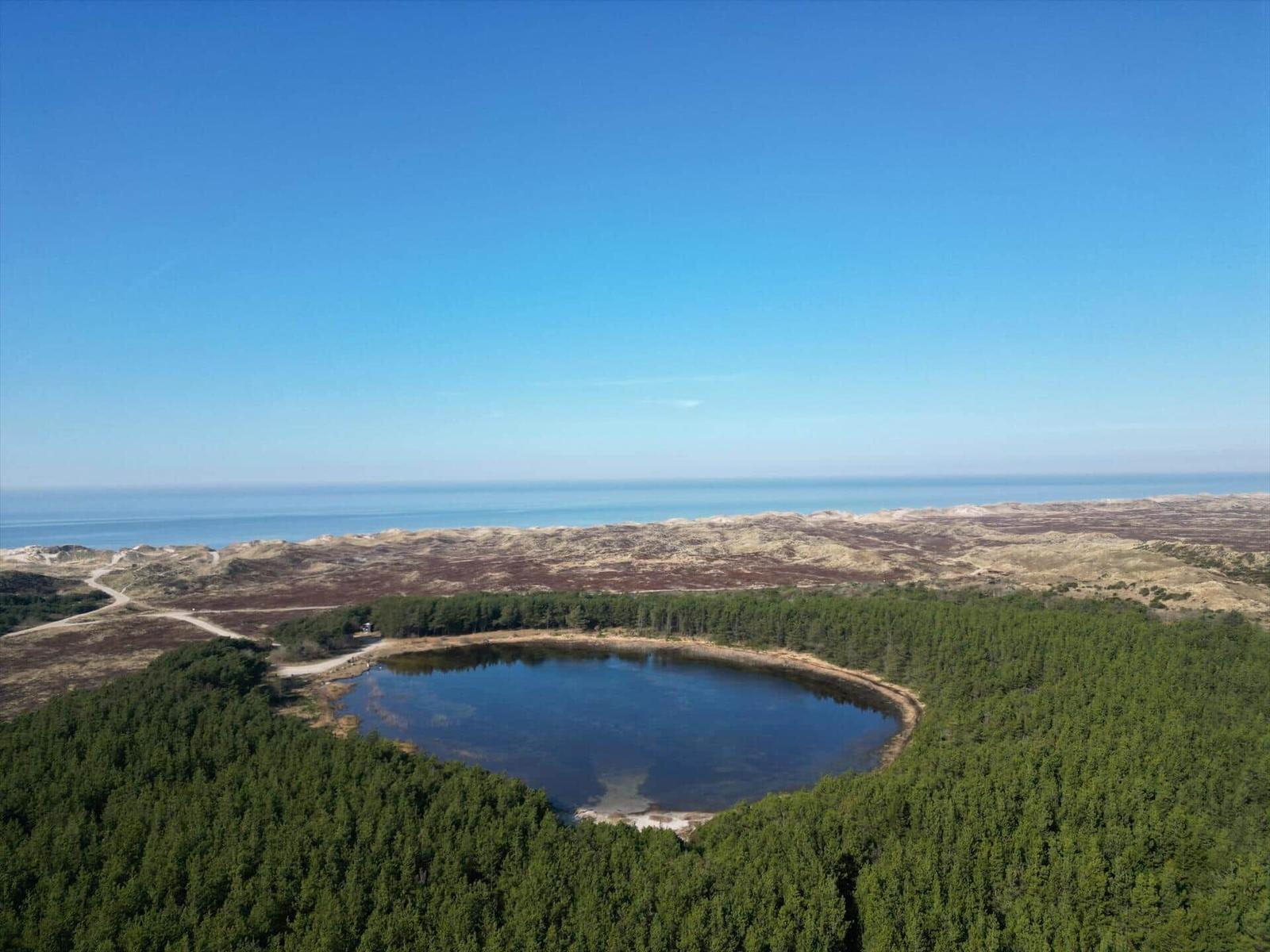 Ein See im Wald mit Blick auf das Meer und Hügel