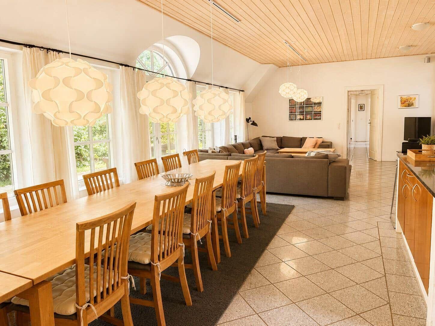 Großer Raum mit Essbereich und Wohnbereich. Holztisch, Stühle, Sofa und hängende Lampen.