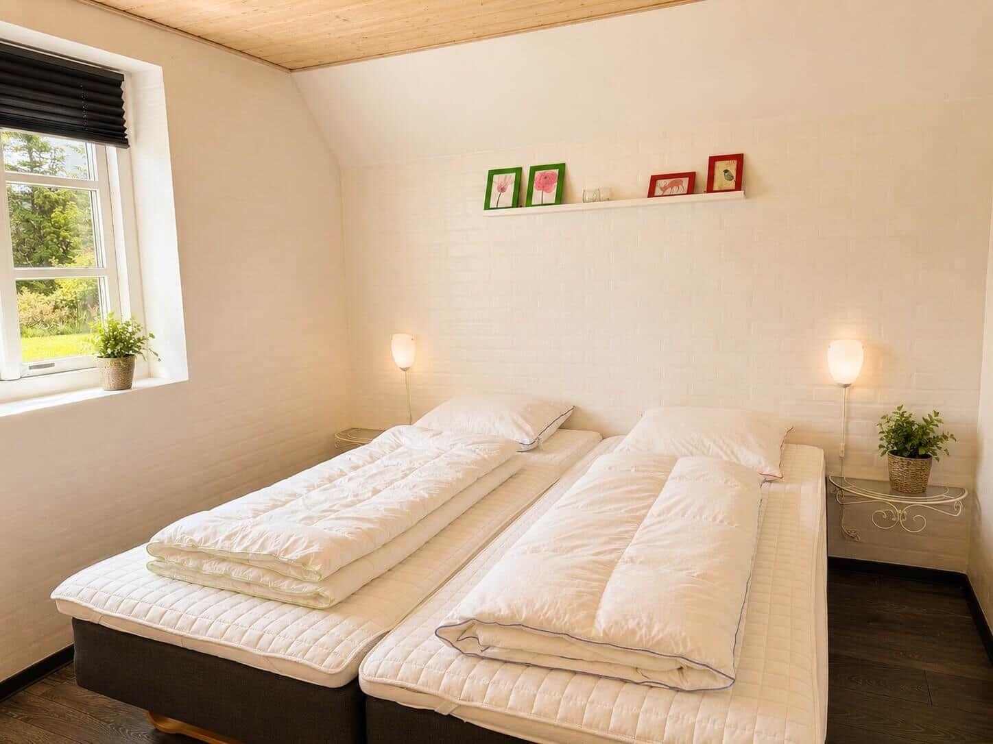 Zwei Betten mit weißen Bettwäschen stehen in einem Raum mit Fenster und Wandregal.