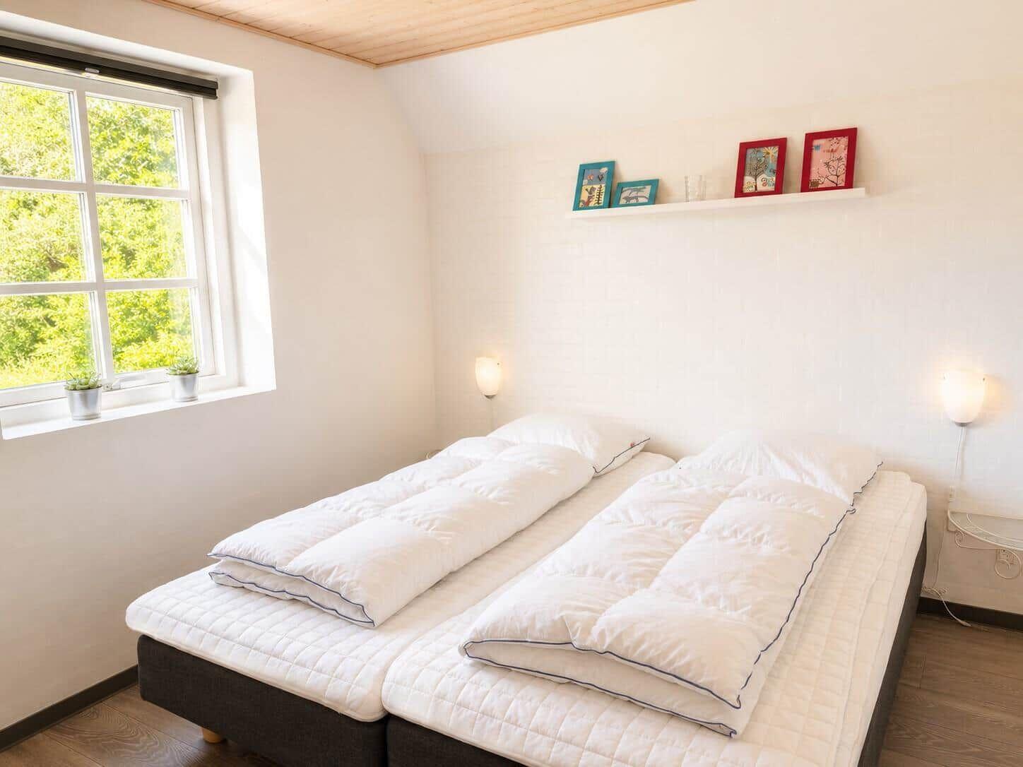 Zimmer mit Doppelbett, Fenster mit Blick auf Grün und Wandregal mit Bilderrahmen.