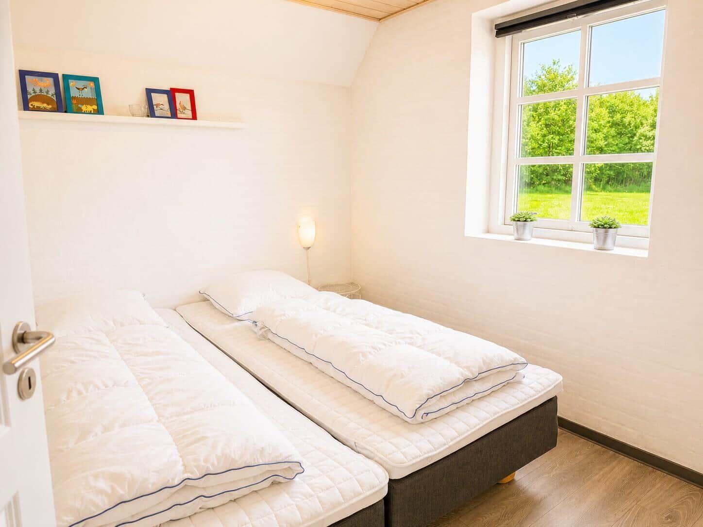 Zwei Schlafplätze mit Matratzen und weißen Bettwäsche. Fenster mit Blick auf grüne Wiese.