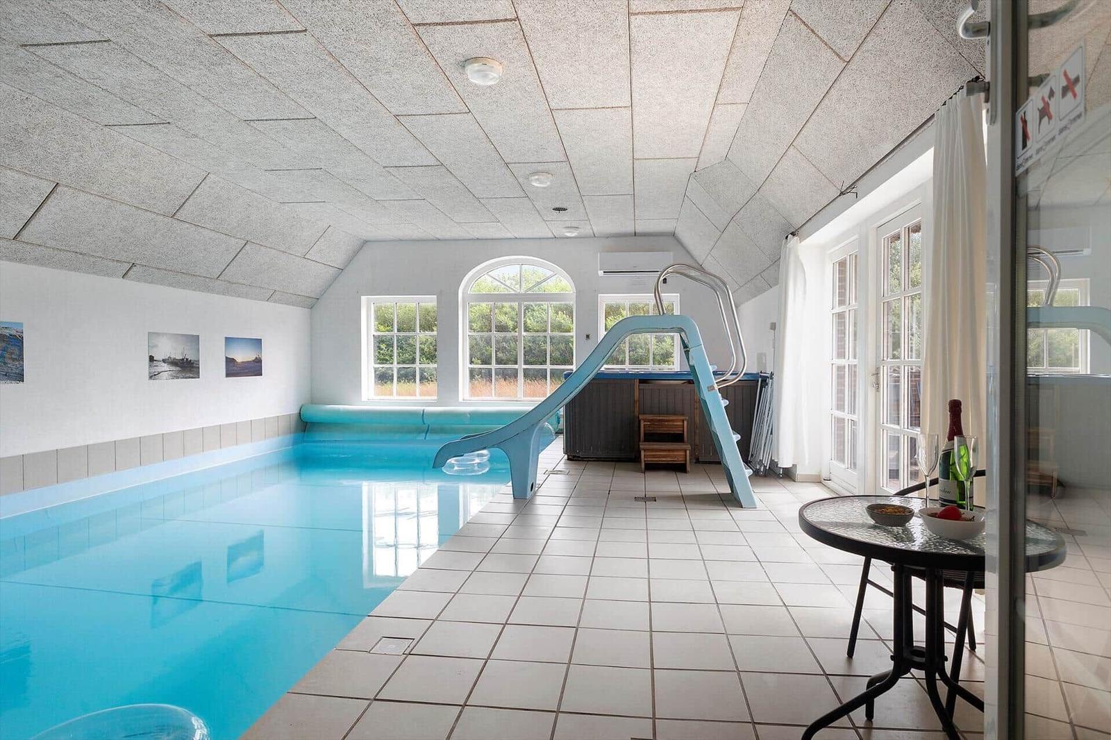 Innenpool mit blauer Rutsche und großen Fenstern. Tisch mit Flasche und Gläsern.