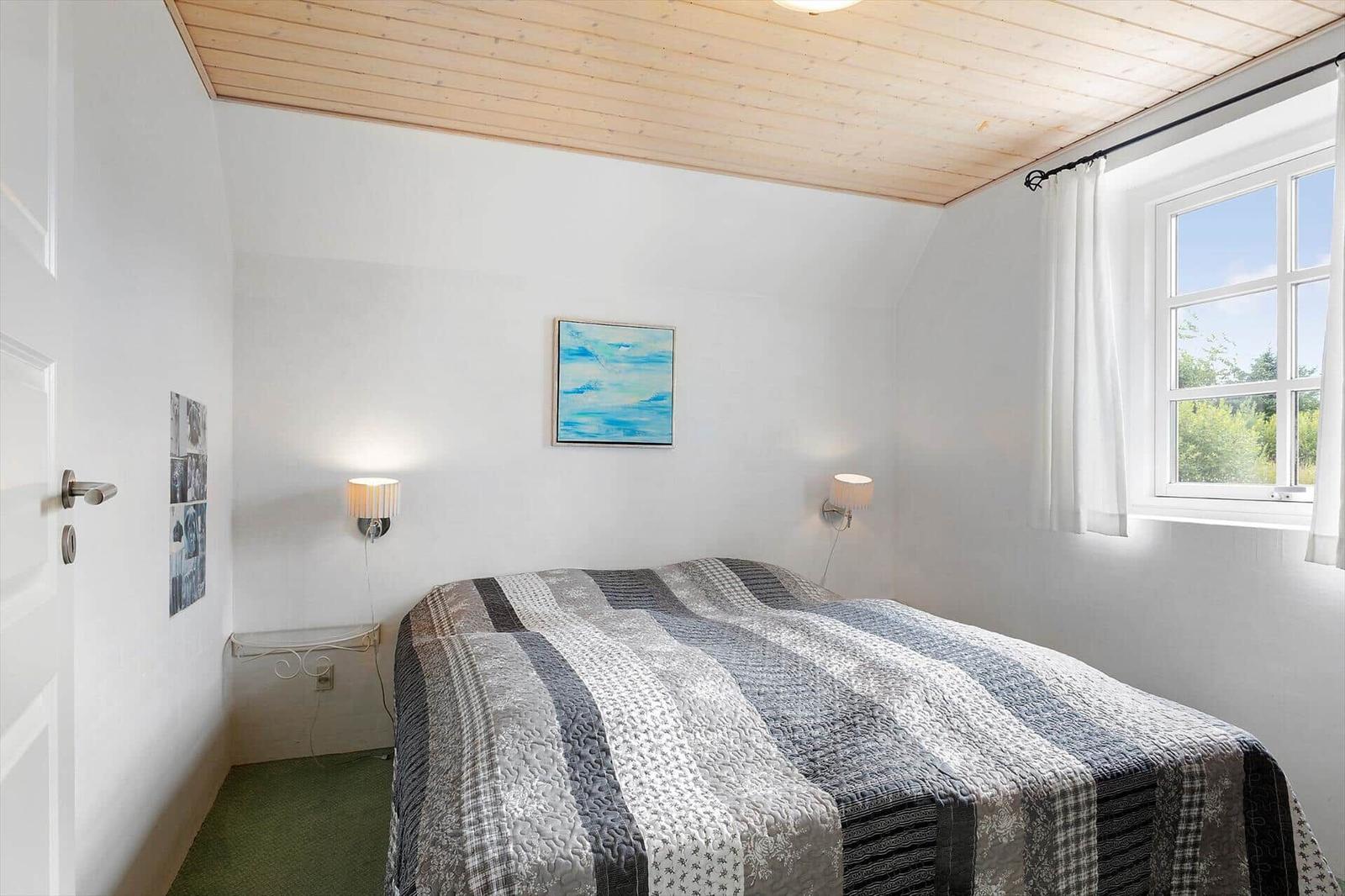Schlafzimmer mit Bett, Wandbild und Fenster. Holzdecke und grüner Boden.