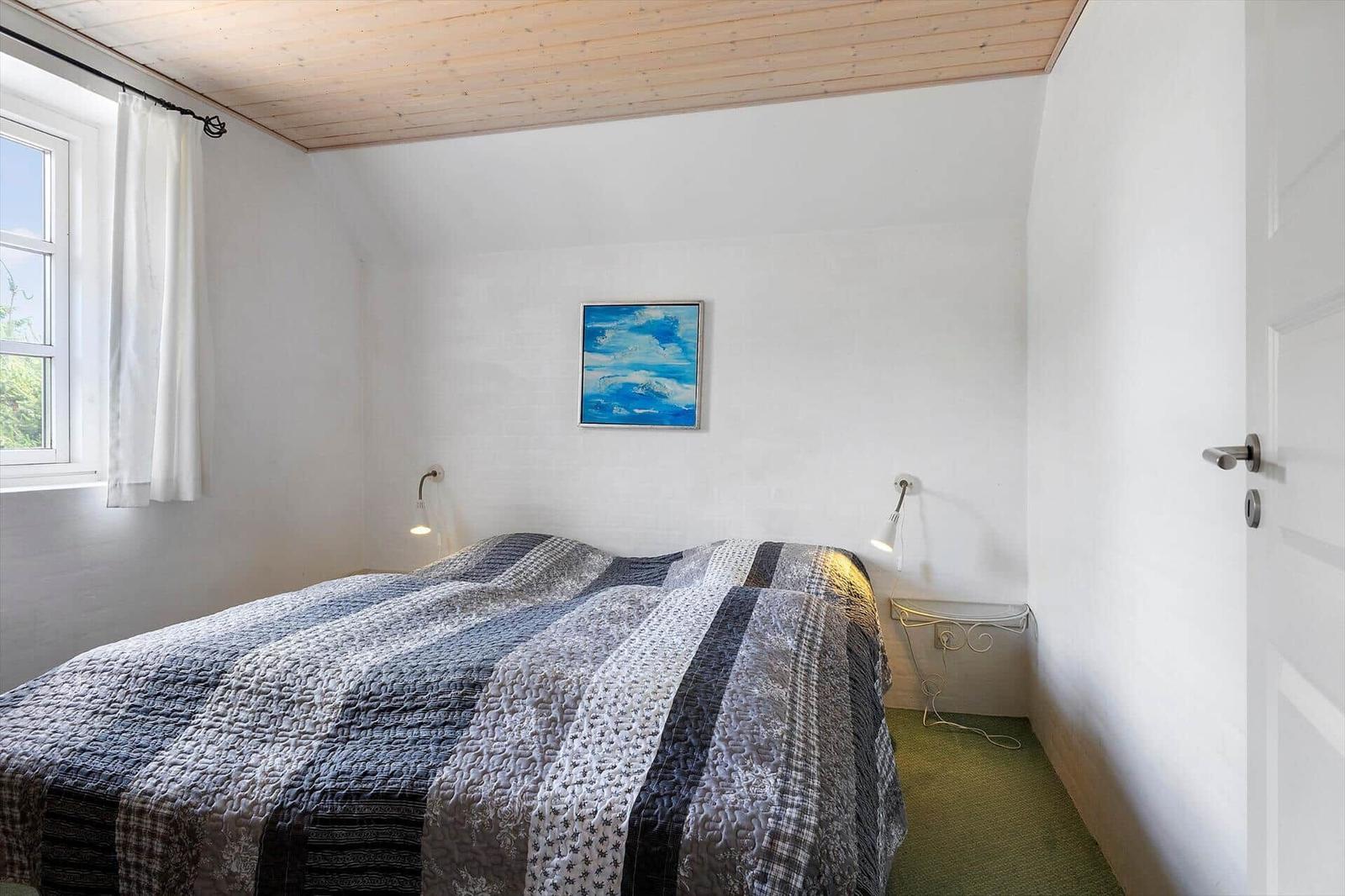Schlafzimmer mit Bett, Fenster, Wandbild und Stehlampe.