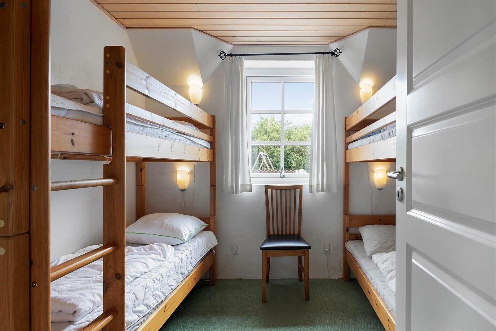 Zimmer mit zwei Doppelstockbetten, Stuhl und Fenster mit Blick auf Grün.