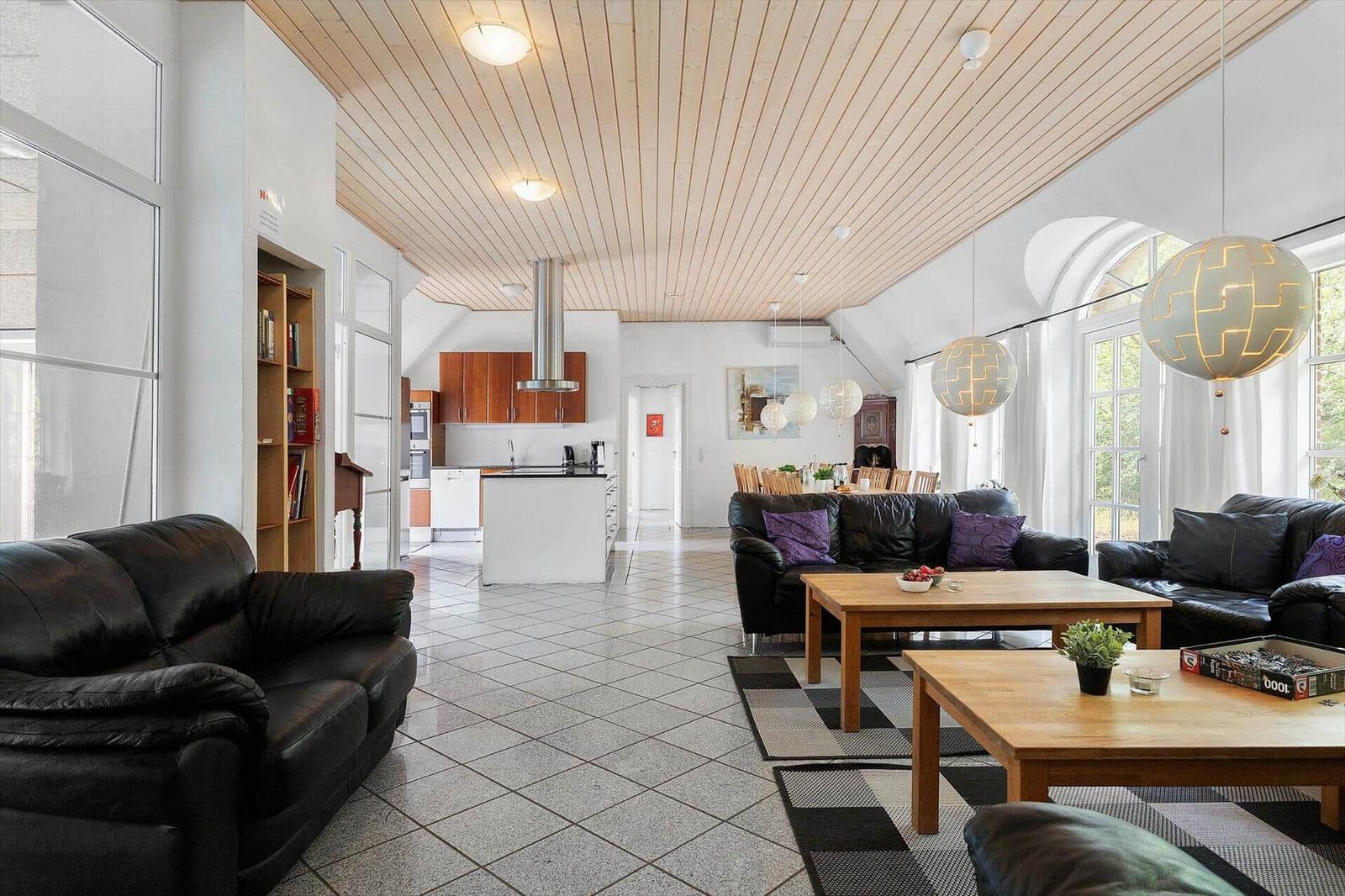 Wohn- und Essbereich mit schwarzen Sofas, Holztischen und hohem Holzdecken