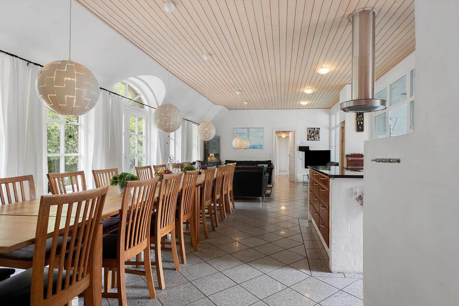 Großer Essbereich mit Holztisch, Stühlen und Deckenleuchten. Küche und Wohnzimmer im Hintergrund.
