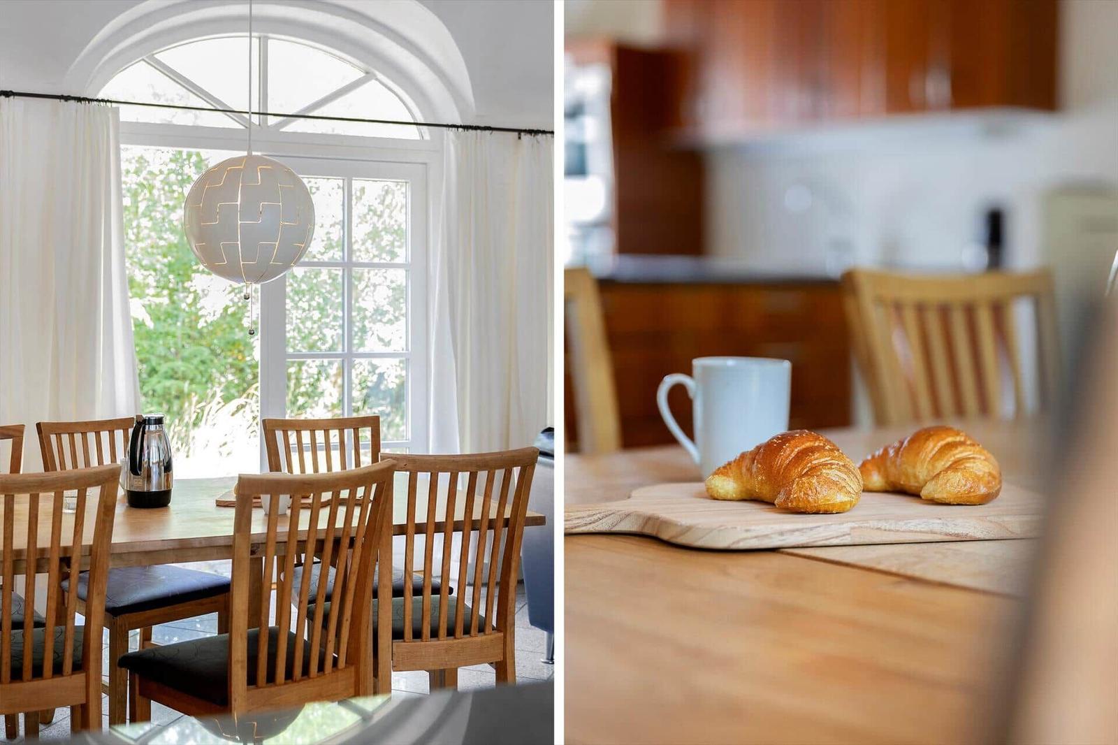Esszimmer mit Holztisch, Stühlen und Fenster. Kaffee und Croissants auf der Theke.