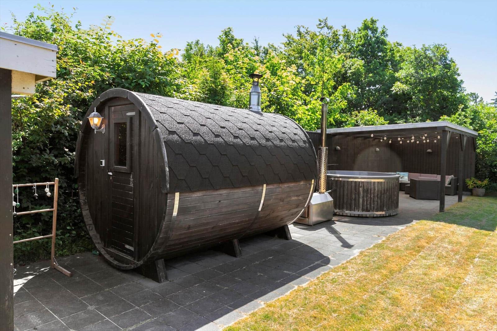 Holzsauna mit Dach und Tür. Nebenher Whirlpool und Sitzbereich im Garten.