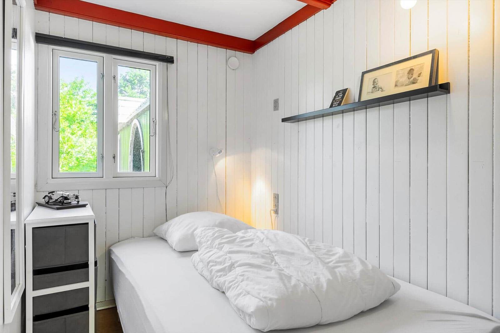 Ein Schlafzimmer mit weißer Holzwand, Bett, Fenster und Regal.