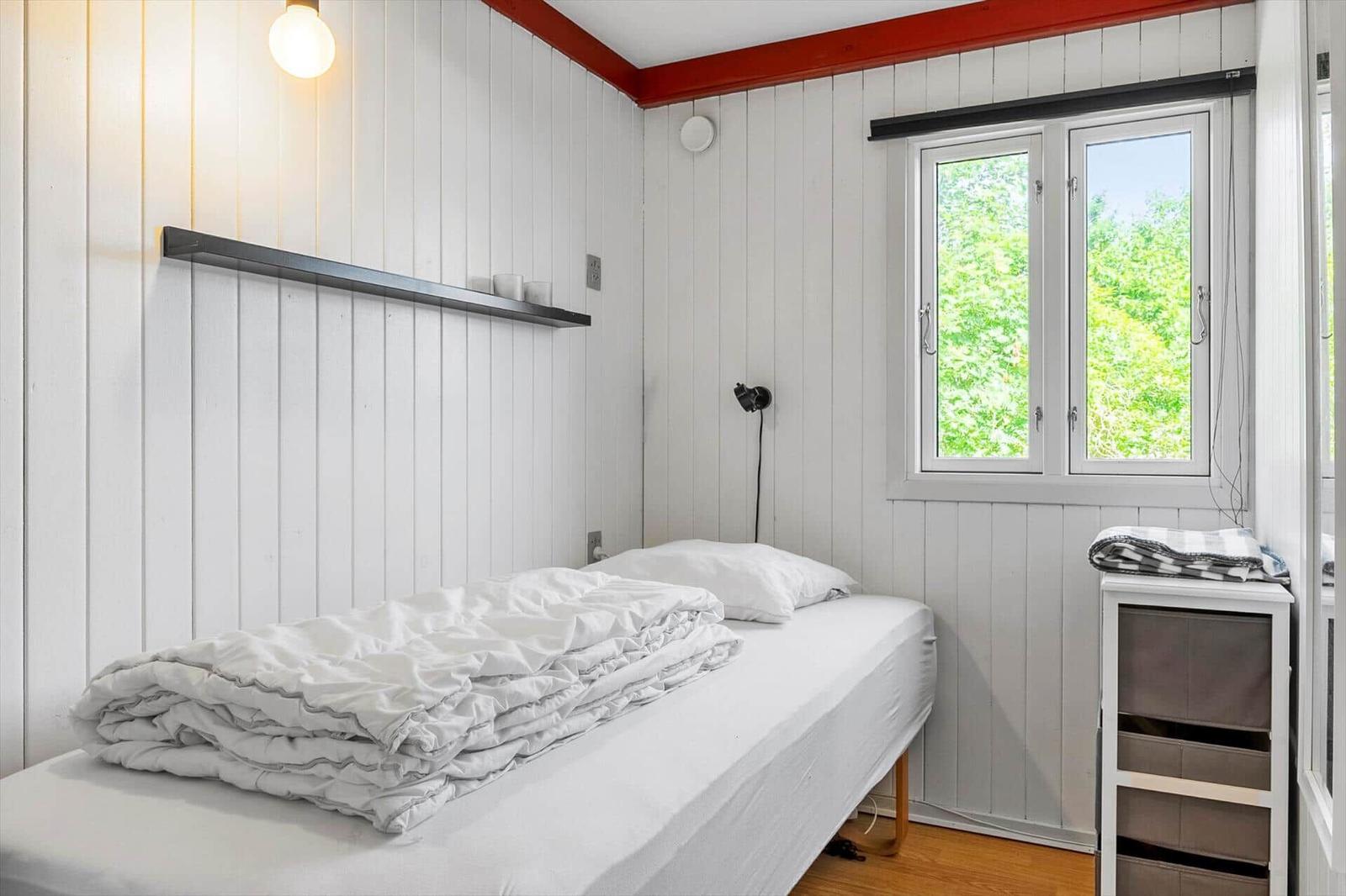 Ein Schlafzimmer mit weißer Wandverkleidung, einem Bett und einem Fenster mit Blick auf Grün.
