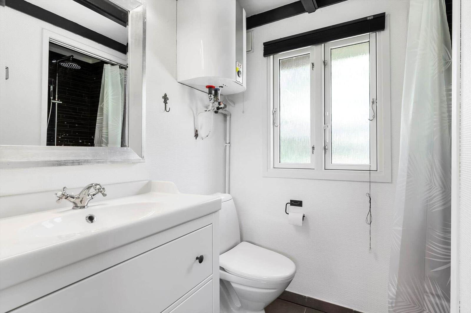 Badezimmer mit Waschbecken, Toilette und Dusche. Fenster und Spiegel sichtbar.