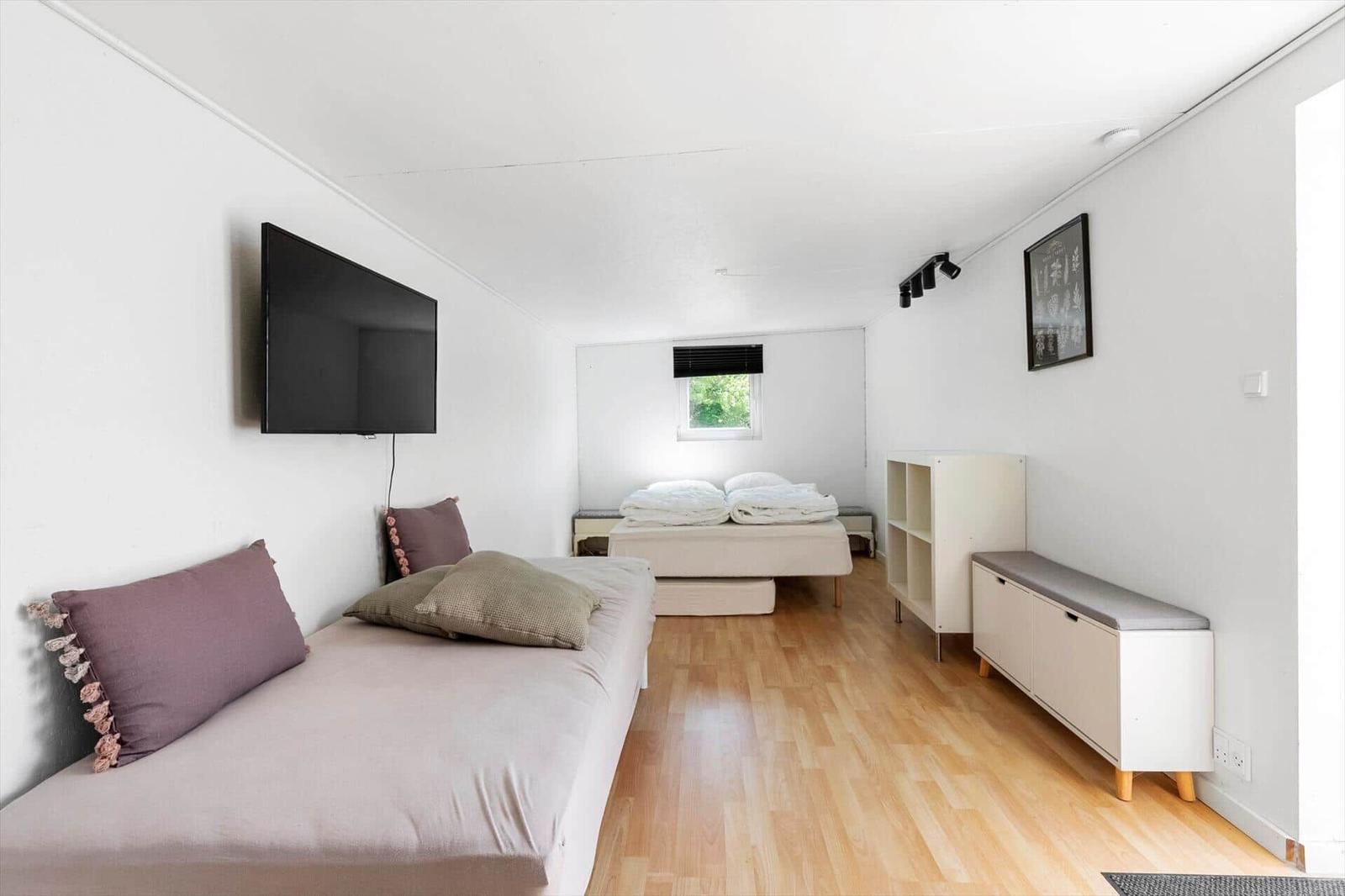Zimmer mit zwei Betten, Wand-TV und Holzboden. Fenster mit Blick auf Grün.