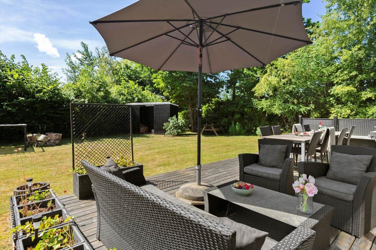 Terrasse mit Sitzgruppe, Sonnenschirm und Grillbereich im Garten.