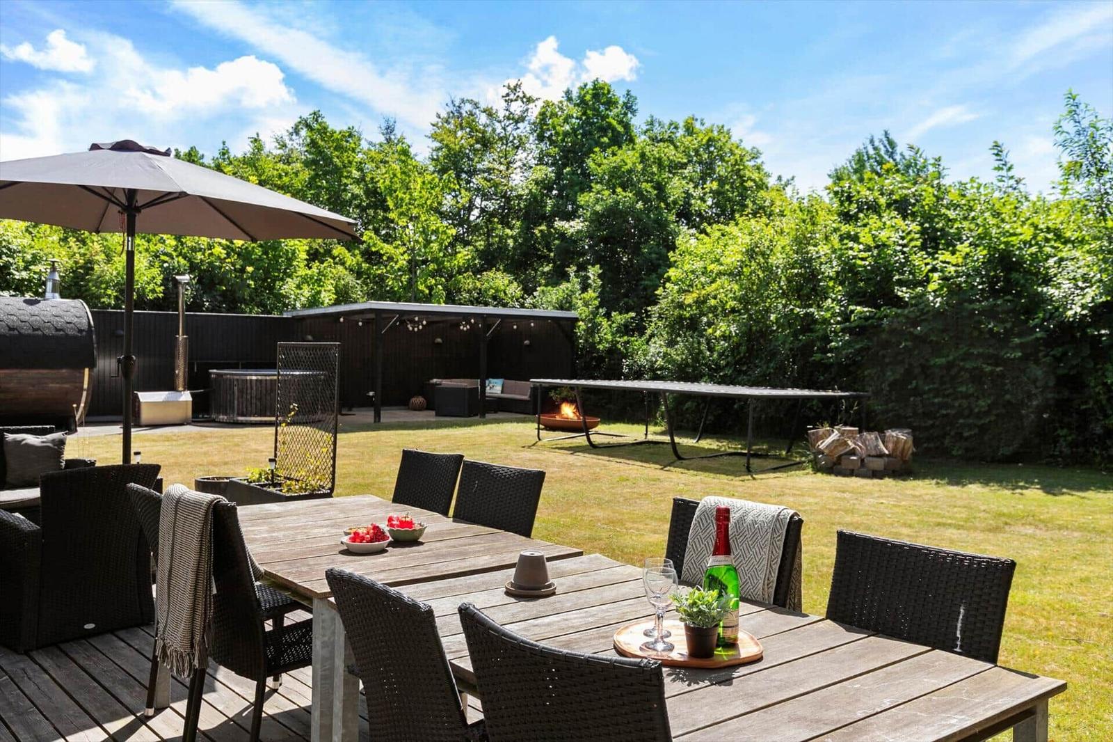 Hinterhof mit Grill, Tisch, Stühlen und Sonnenschirm. Grasfläche und Bäume im Hintergrund.
