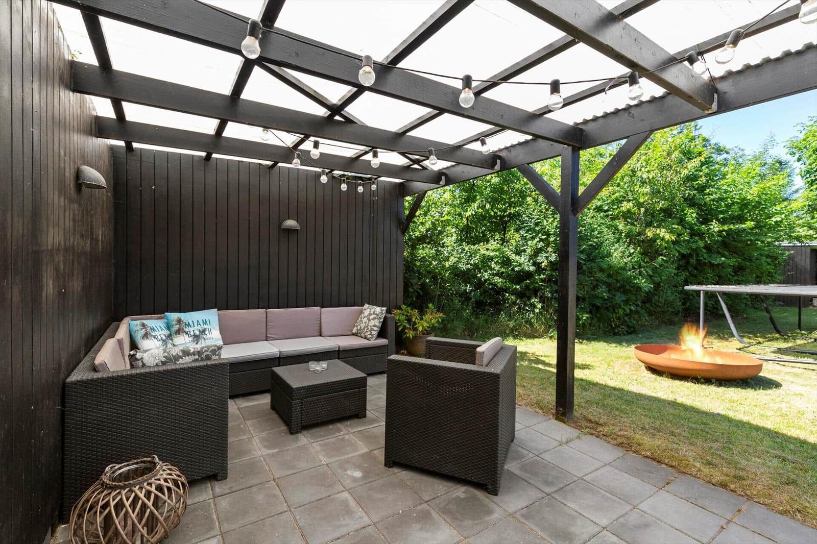 Terrasse mit Sitzgruppe, Feuerkorb und Beleuchtung unter einer Markise.