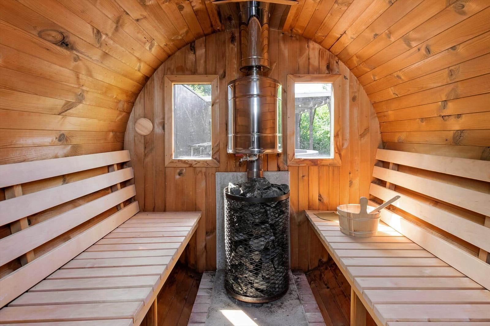 Sauna mit Holzbank, Holzwand und Ofen mit Steinen.