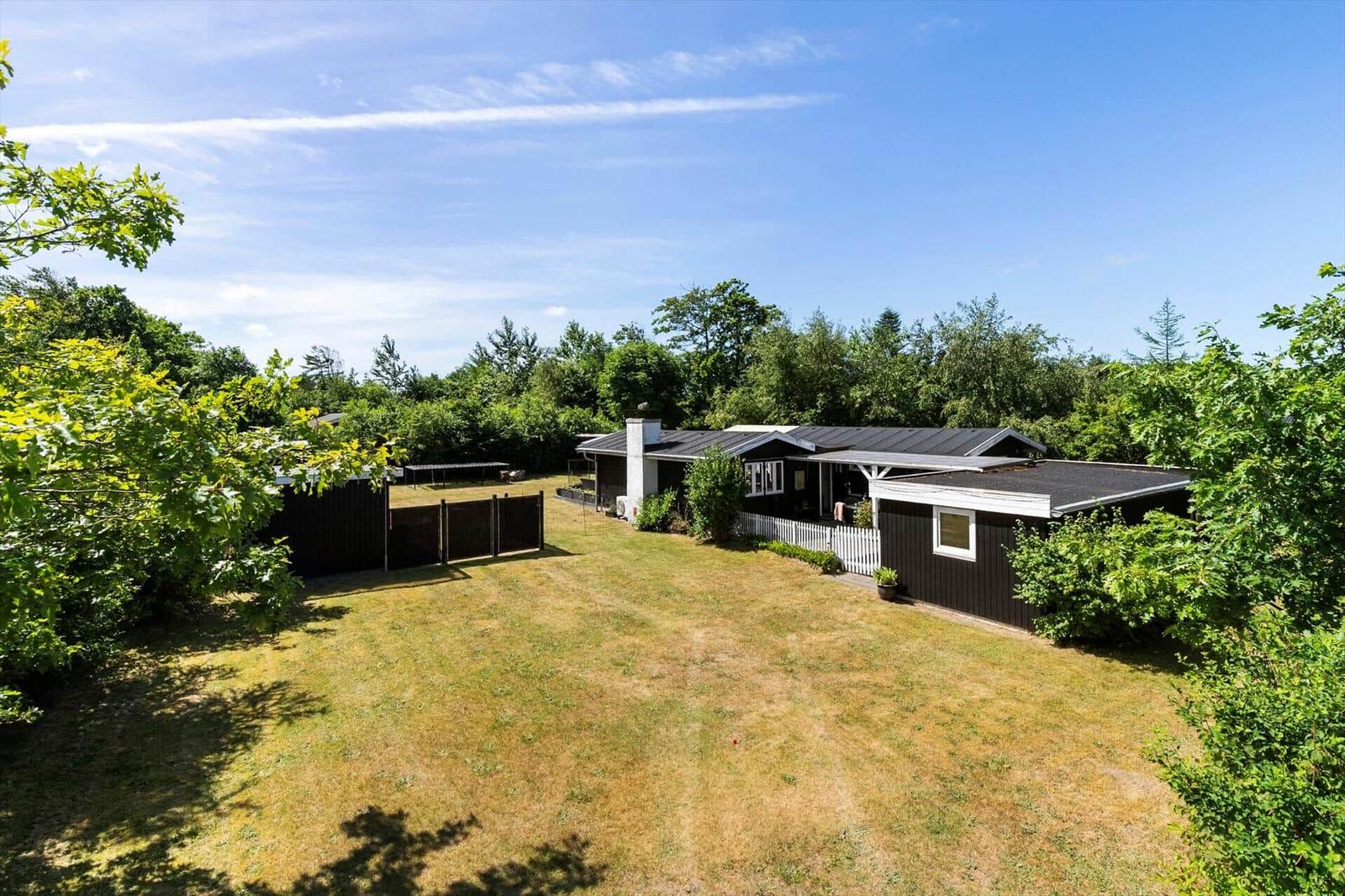 Haus mit Garten und Wald im Hintergrund unter blauem Himmel.