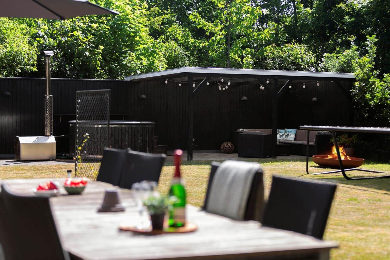 Hinterhof mit Grill, Sitzgelegenheiten und Feuerkorb. Tisch mit Flasche und Obst.