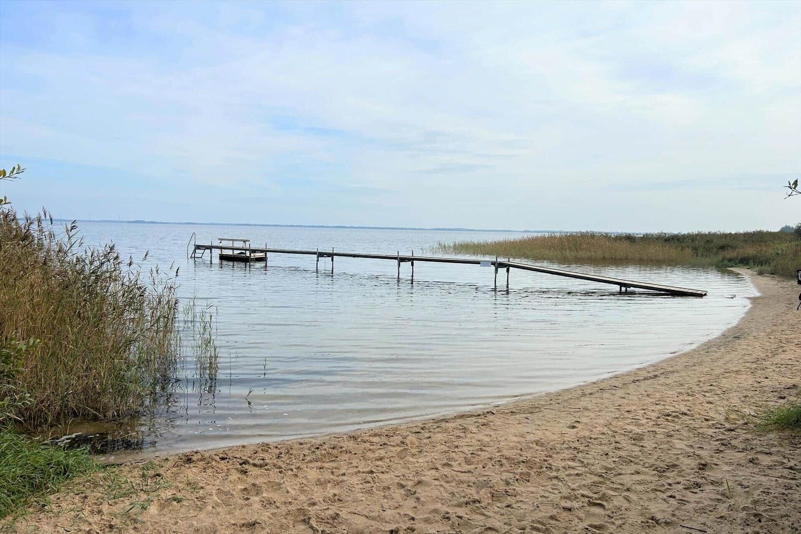 Ein hölzerner Steg führt vom Strand in einen ruhigen See.