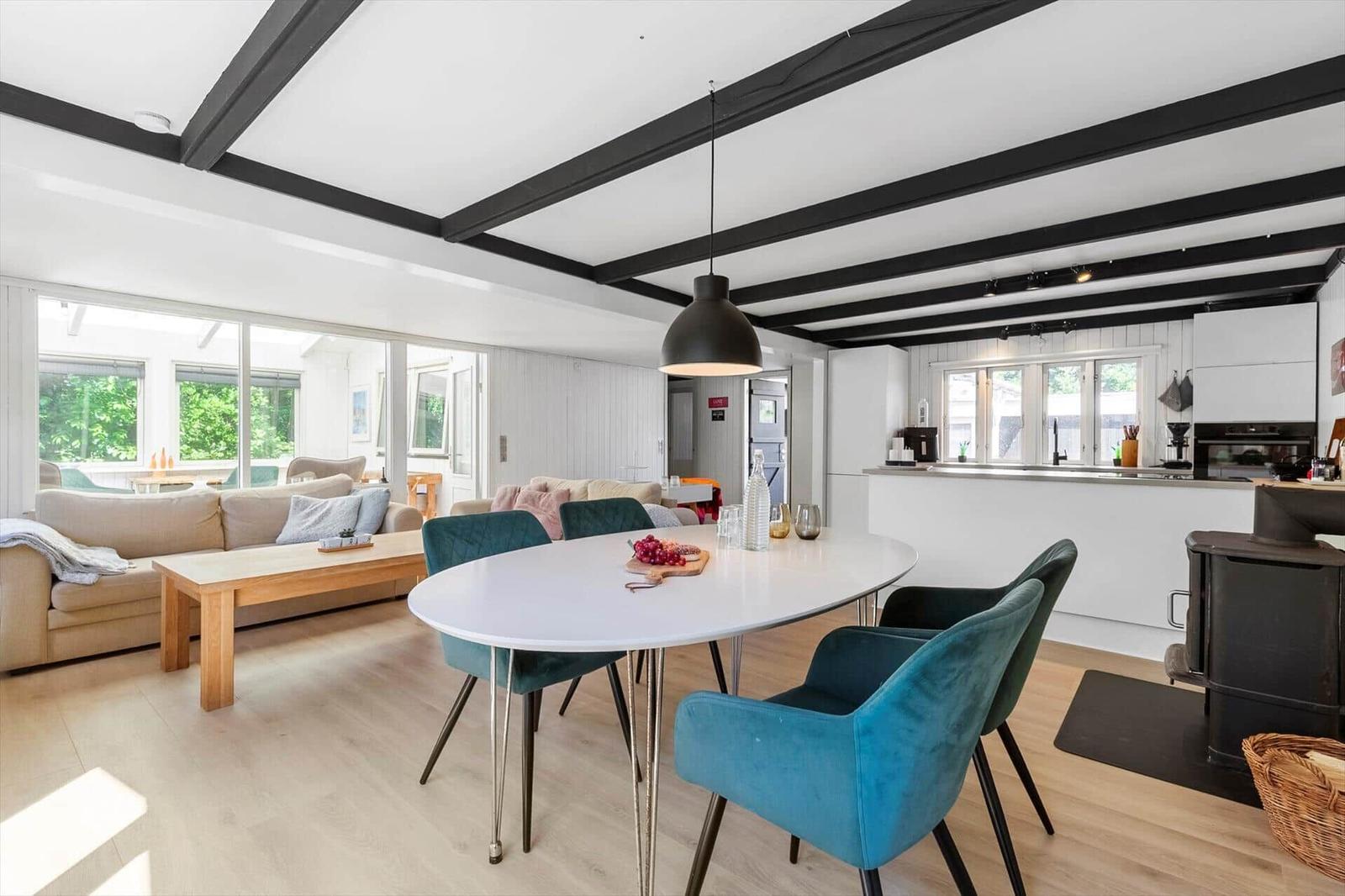 Essbereich mit blauen Stühlen und weißem Tisch. Wohnbereich mit Sofa und Holztisch. Küche mit Arbeitsplatte.