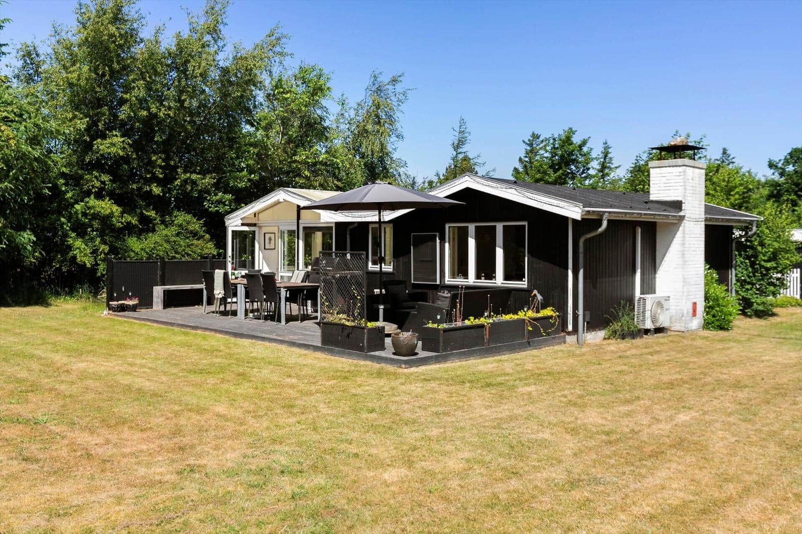 Haus mit Terrasse, Garten und Grillplatz unter blauem Himmel.