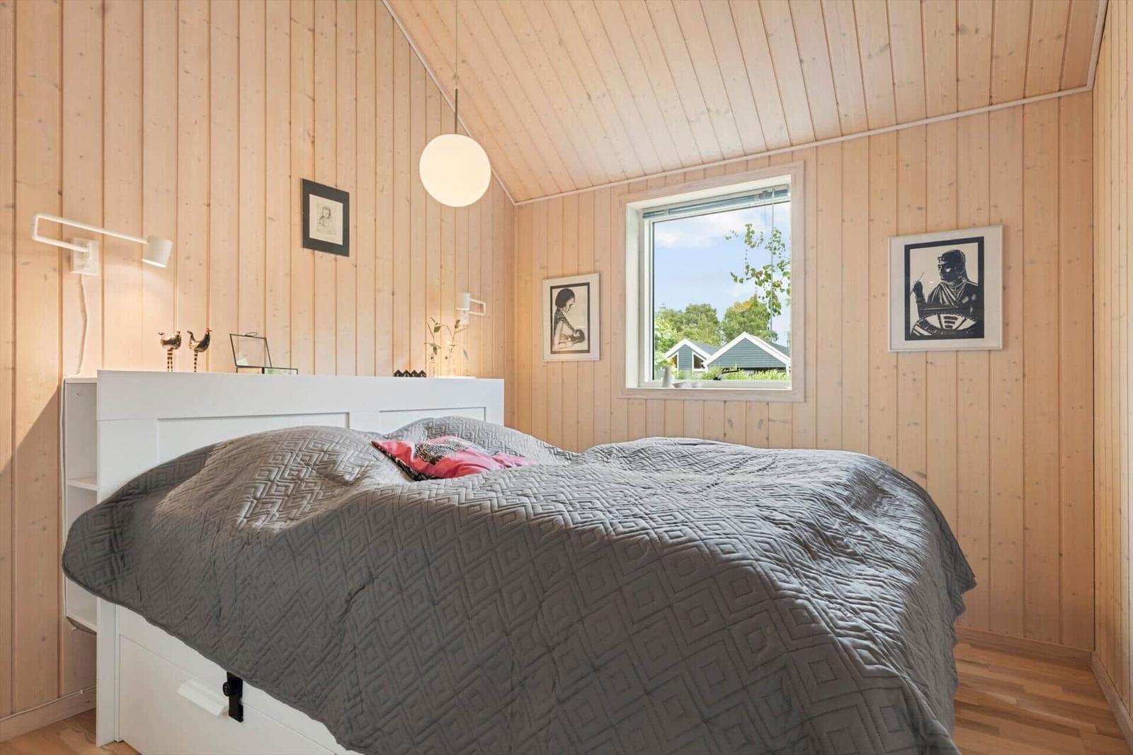 Schlafzimmer mit Holzwand, weißem Bett und Fenster mit Blick auf Außenbereich.