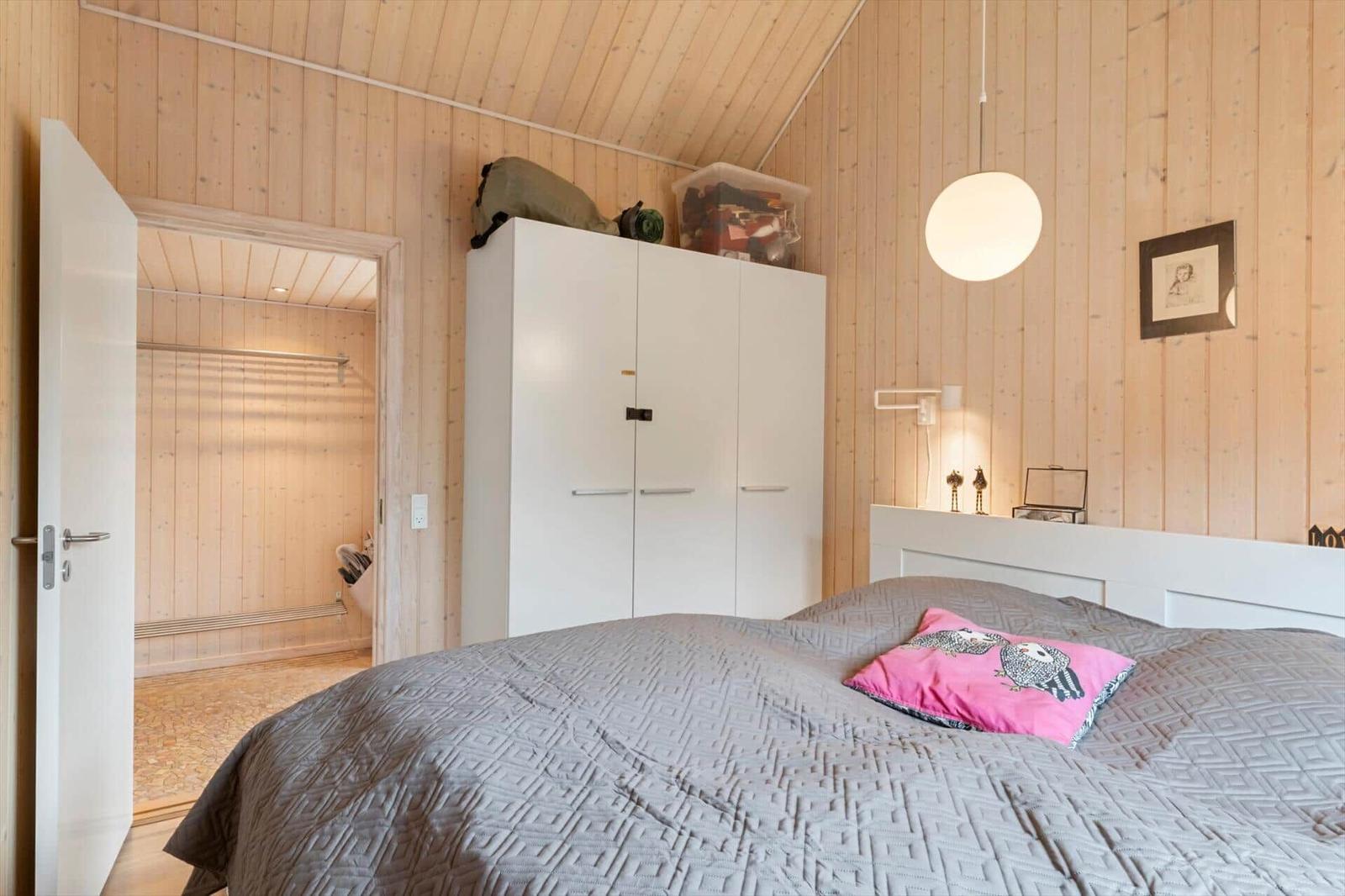 Schlafzimmer mit Holzwand, weißem Schrank und Bett mit Kissen.